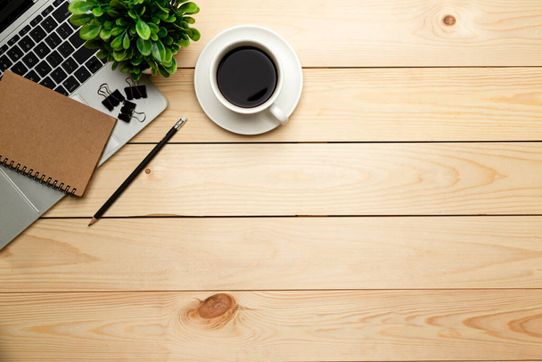 Kancelářský stůl s výhledem shora. Pracovní plocha s prázdnou, kancelářské potřeby, notebook, tužka, zelený list, a šálek kávy na dřevěném pozadí. - Fotografie, Obrázek