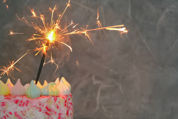 close-up on a dark background a cake with a lit sparkler. Concept - holiday, celebration, birthday. Horizontal photo, copy space. - Foto, imagen