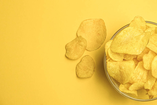 Potato chips in a round bowl on a yellow background. Space for text on the left. Top view. The most popular snack. Junk food. - Fotografie, Obrázek