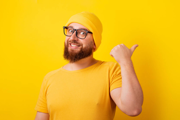 usmívající se muž ukazuje palec nahoru gesto a ukazuje na prázdné místo přes žluté pozadí - Fotografie, Obrázek