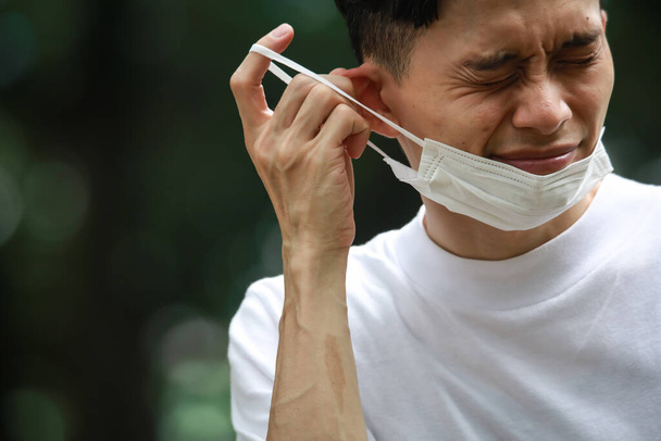 Um homem usando uma máscara e tendo uma orelha dolorida - Foto, Imagem