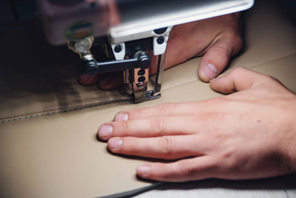 Werkproces van lederen vakman. Tanner naait leer op een speciale naaimachine, close-up. Werknemer naaien lederen product op de naaimachine. Werkplaats voor leerarbeiders. - Foto, afbeelding
