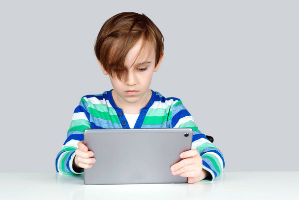 Iskolásfiú otthon tanul. Gyermekek, technológia és oktatási koncepció. Aranyos, komoly gyerek digitális táblagéppel. Online iskola, modern technológia. Okos fiú táblagép az online leckét. - Fotó, kép
