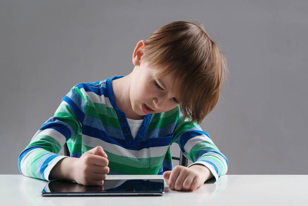 Nervous boy studying online with laptop. Upset child has problem with gadget. Negative emotions during online lesson. Education, online learning and gaming at home. Angry boy hitting his tablet. - Photo, Image