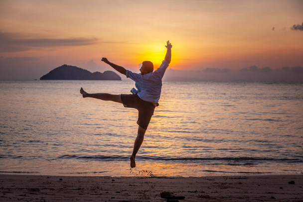 Silhouette Young man jumping having joy on the tropical beach at sunset - Zdjęcie, obraz