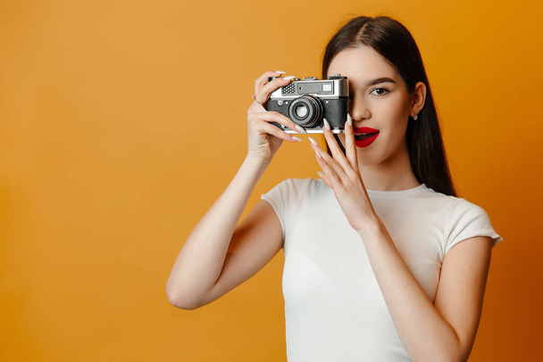 Beautiful girl is taking photos against the bright background. The girl has straight black hair and red lips - Foto, imagen