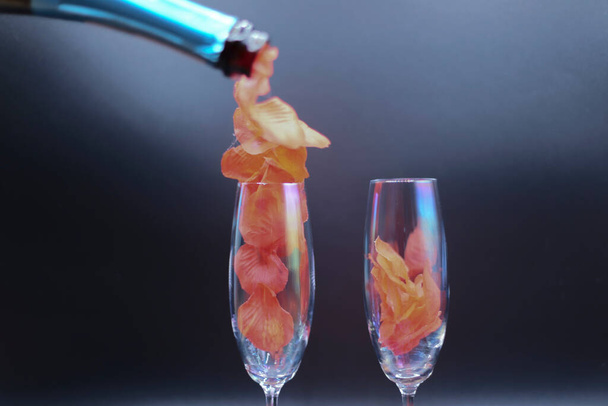 una bottiglia di spumante versa dei petali di rose in un bicchiere - Foto, Bild