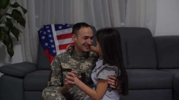 Figlia felice bambina con bandiera americana abbracciare il padre in uniforme militare è tornato dall'esercito degli Stati Uniti, soldato maschio riunito con la famiglia a casa - Filmati, video