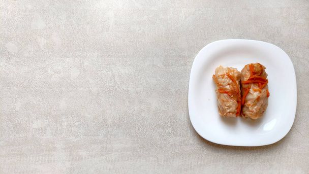 White plate with cabbage rolls top view, on a textured table, place for text near the dish. Homemade food, simple food. - Photo, image
