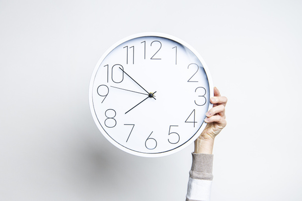  Woman's hand holds a large white clock on a light background  - Photo, Image