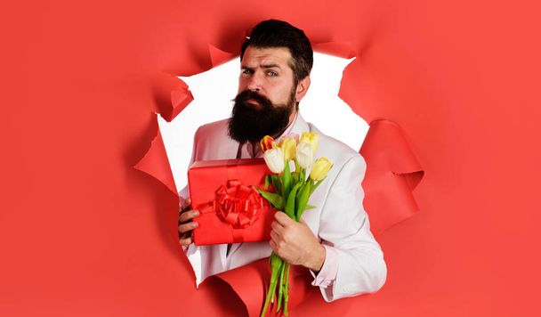 花束とギフトボックスを持つ髭の男。現在とチューリップを持つロマンチックな男性。バレンタインデー、レディースデー. - 写真・画像