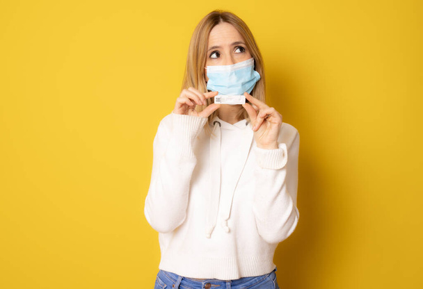 Νεαρή γυναίκα με χειρουργική μάσκα που δείχνει δοκιμασία απομονωμένη σε κίτρινο φόντο. - Φωτογραφία, εικόνα