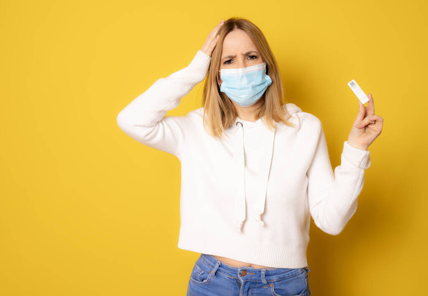 Young woman wearing surgical mask showing a test isolated over yellow background. - Photo, Image