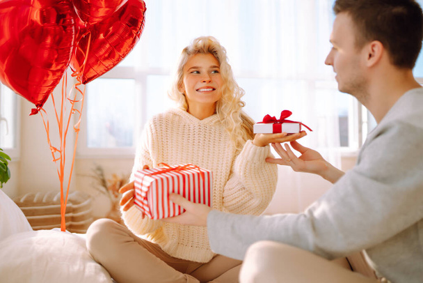 Beautiful young couple at home celebrating Valentine's Day. Lovers give each other gifts. Hug, kiss and enjoy spending time together. - Valokuva, kuva