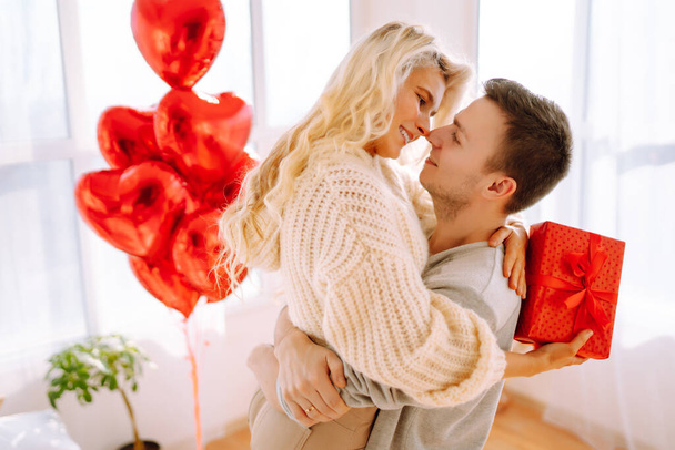 Beautiful young couple at home celebrating Valentine's Day. Lovers give each other gifts. Hug, kiss and enjoy spending time together. - Φωτογραφία, εικόνα