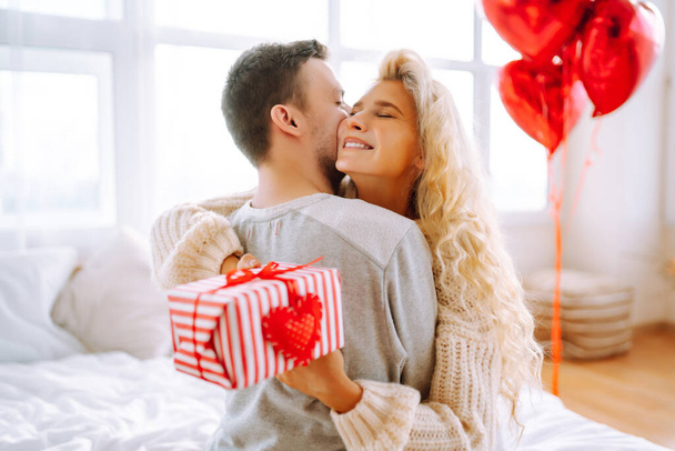 Beautiful young couple at home celebrating Valentine's Day. Lovers give each other gifts. Hug, kiss and enjoy spending time together. - Foto, immagini