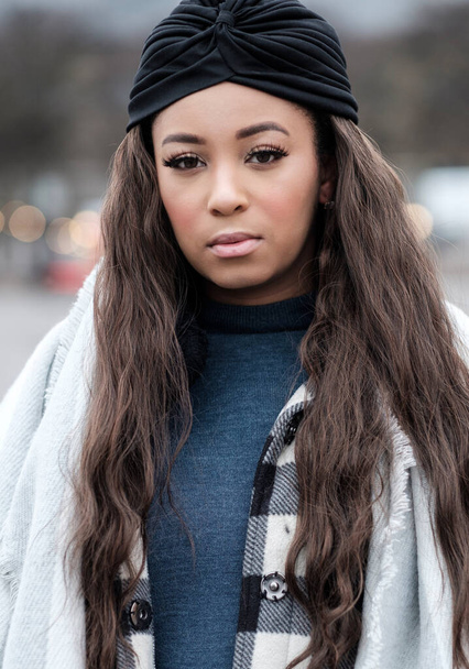 Portrait of young black woman looking to camera. She is wearing a black cap, scarf and a coat. Very cold winter morning. - Foto, Imagem