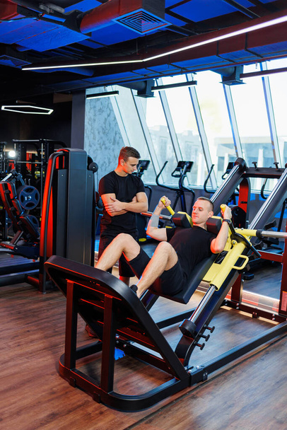 Athletic man doing exercises with the help of his personal trainer in a public gym. - Valokuva, kuva