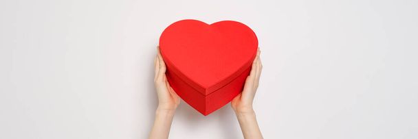 Manos sosteniendo una gran caja roja en forma de corazón. Banner de vídeo de moda para el Día de San Valentín, Día Internacional de la Mujer o el día de las madres. Primer plano de la bandera - Foto, imagen