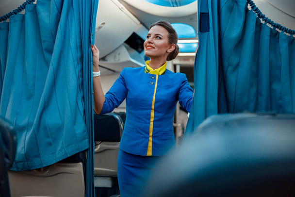 Vreugdevolle vrouw stewardess houdt gordijnen in passagiersvliegtuig - Foto, afbeelding