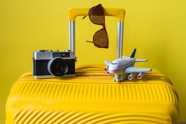 yellow suitcase, camera, glasses and plane - traveler's accessories on a yellow background. travel concept - Photo, image