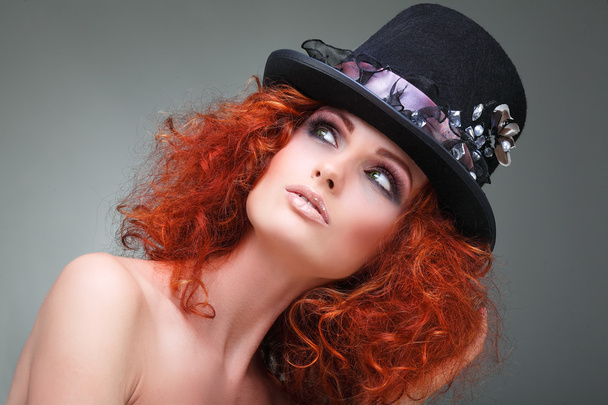 szép szexuális vörös hajú lány egy fekete kalapot, szürke háttéren portréja. tartozékok. - Fotó, kép