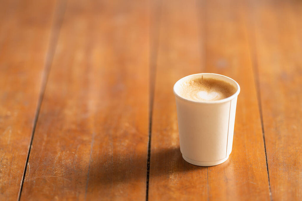 Крупный план одноразового бумажного чашечки горячего кофе латте с искусством формы сердца пену молока на старом деревянном столе. - Фото, изображение