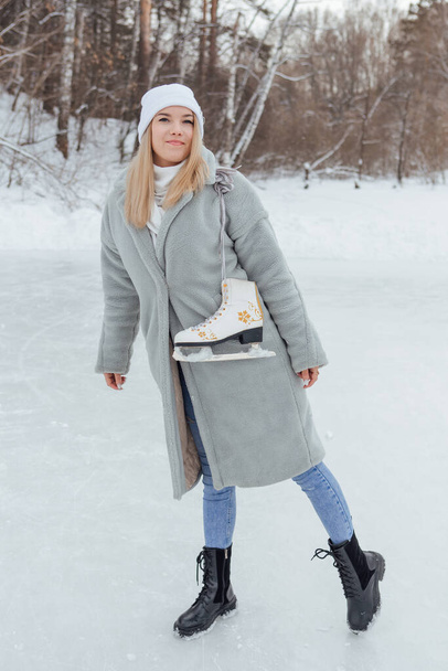 Lovely young woman with ice skates on the ice rink. Girl is going to skating on ice in a winter frosty day - Foto, afbeelding