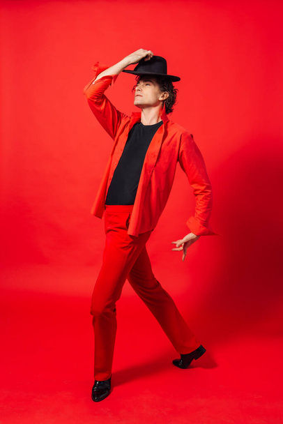 Portrait of a tall handsome man dressed in red shirt and black hat posing on the red background. - Foto, Imagem