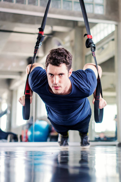 Deportista o hombre guapo haciendo ejercicio con correas de fitness para fortalecer su músculo abdominal en el gimnasio. - Foto, imagen