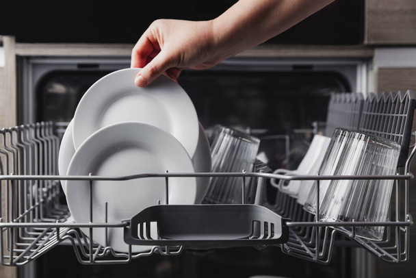 Άνοιγμα πλυντηρίου πιάτων με καθαρά μαχαιροπήρουνα, ποτήρια, πιάτα μέσα στην κουζίνα του σπιτιού - Φωτογραφία, εικόνα