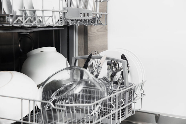 Lavavajillas abierto con utensilio limpio en el interior, cubiertos, vasos, platos en la cocina - Foto, imagen
