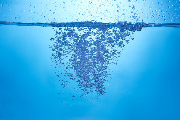 Blue background with water bottle falling in and multiplle drops and splashed. Water bubbles texture - Photo, Image