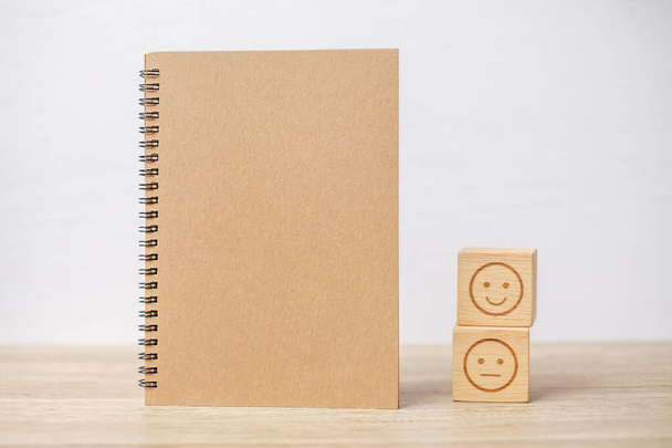 emotion face block and notebook on table. Emoticon for customer review, satisfaction, mood, mental health and feedback concept - Photo, Image