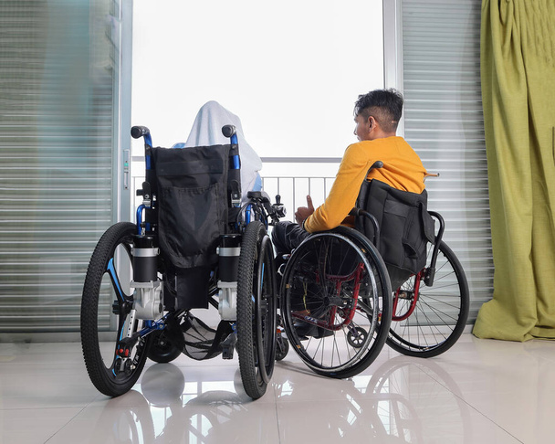 Południowo-wschodniej Azji malajski mężczyzna kobieta para chusta Tudung średni wiek niepełnosprawnych na wózku inwalidzkim patrząc przed balkonem okno patrzeć na zewnątrz trzymając się za rękę - Zdjęcie, obraz