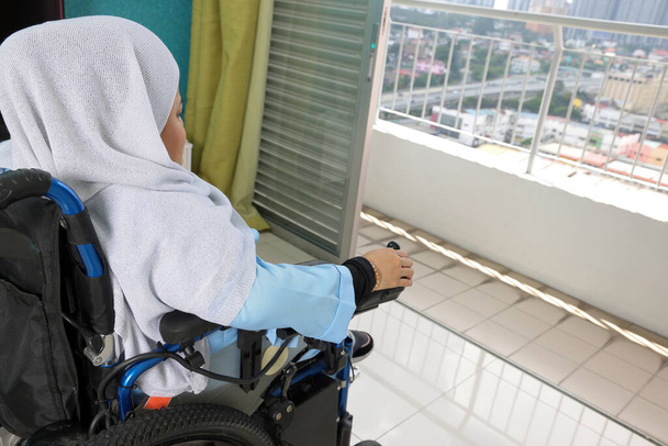 Południowo-wschodniej Azji malajski chusta Tudung średnim wieku niepełnosprawna kobieta na wózku inwalidzkim patrząc siedzi przed oknem balkonu wyjrzeć na zewnątrz zbliżenie strony - Zdjęcie, obraz