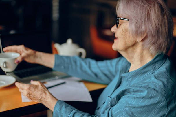 Belle femme âgée mature avec des lunettes s'assoit à une table devant un ordinateur portable Réseaux sociaux inchangés - Photo, image