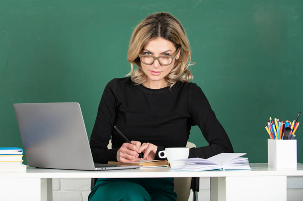 Serious concentrated teacher. Portrait of smart young woman in glasses with book on the blackboard in class at high school or collage. Female student study in university. - Photo, Image