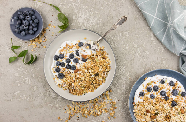 two plates of walnut granola or homemade muesli on a gray concrete background. ripe blueberries in a bowl for a well-cured meal. top view - Foto, afbeelding