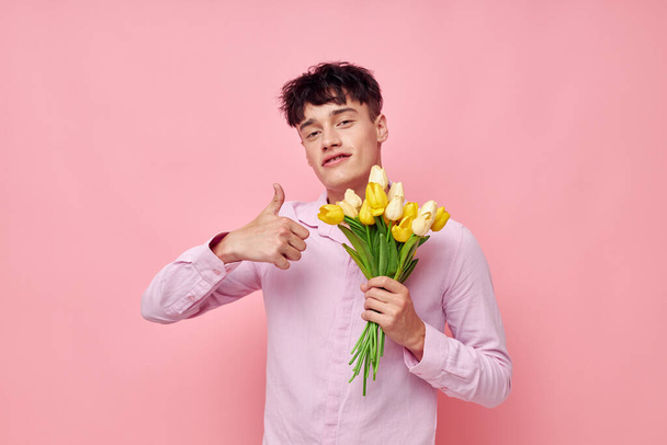portrait of a young man in a pink shirt with a bouquet of flowers gesturing with his hands model studio - Photo, Image