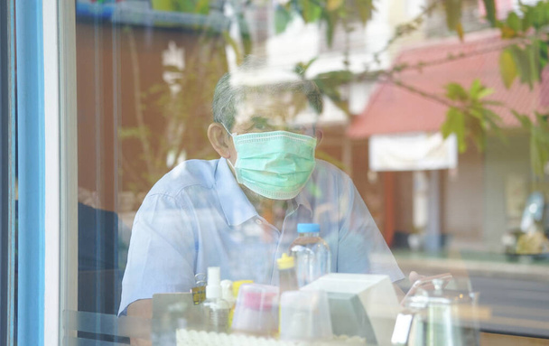 старший мужчина носить защитную маску для лица, сидя в ресторане вид через стекло окна                                 - Фото, изображение