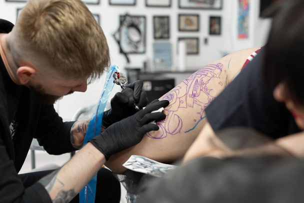 Artista profesional del tatuaje hace un tatuaje en una pierna de chicas jóvenes
. - Foto, Imagen