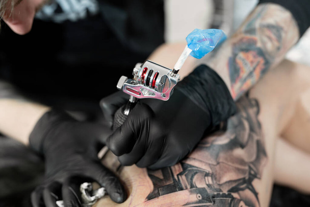 Close up image of the bearded tattoo male artist makes a tattoo on a female leg. - 写真・画像