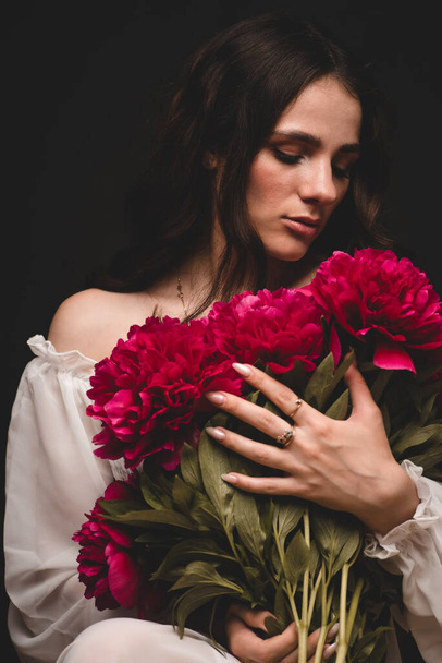 portrait d'une jeune femme sensuelle avec un bouquet de pivoines rouges à la main - Photo, image