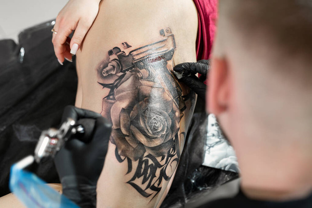 Close up image of the bearded tattoo male artist makes a tattoo on a female leg. - Zdjęcie, obraz