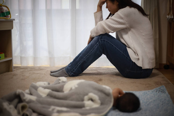 jovem estressado mulher sentado no chão enquanto bebê deitado perto por - Foto, Imagem