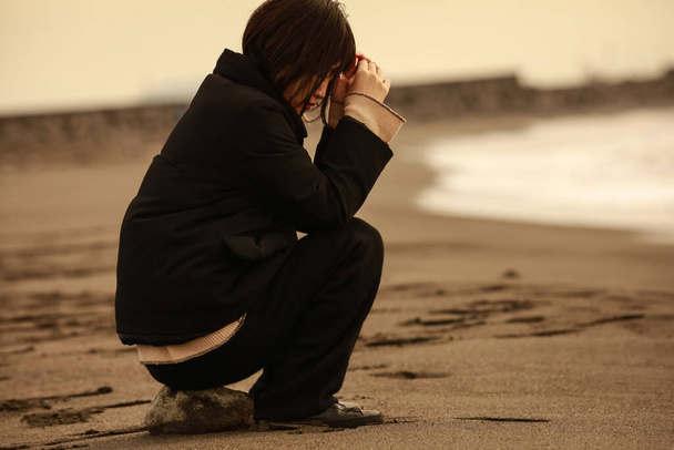 fiatal depressziós nő ül a kövön a homokos tengerparton naplementekor - Fotó, kép