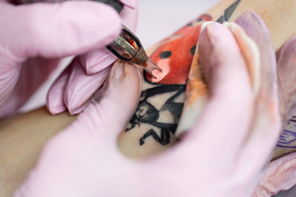Close-up of a tattoo artist doing a tattoo on the leg of a young girl in the salon. Professional tattooist doing tattooing in studio. - Fotó, kép