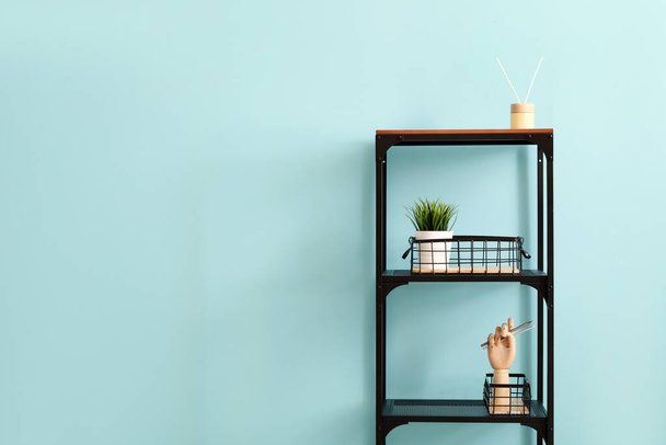 Shelf unit with reed diffuser, houseplant and wooden hand near color wall - Photo, Image