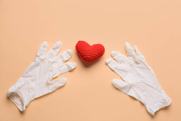 Ιατρικά γάντια και κόκκινη καρδιά στο φόντο χρώμα. Έννοια δωρεάς - Φωτογραφία, εικόνα